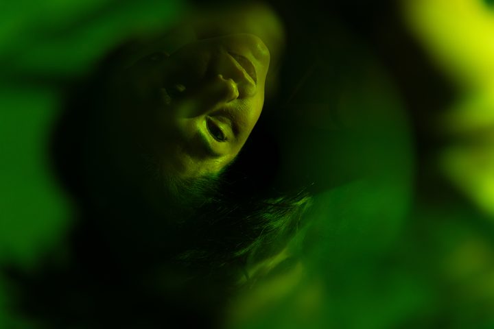 A figure low to a mirrored floor in warm amber and green strobe, the reflection doubling the light back beneath the body.