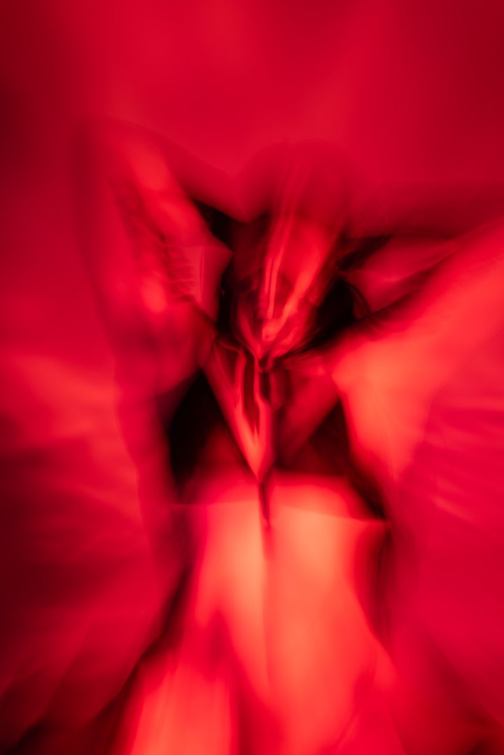 A spectacular red frame, the figure caught in radiating streaks of long-exposure light against a deep crimson ground.