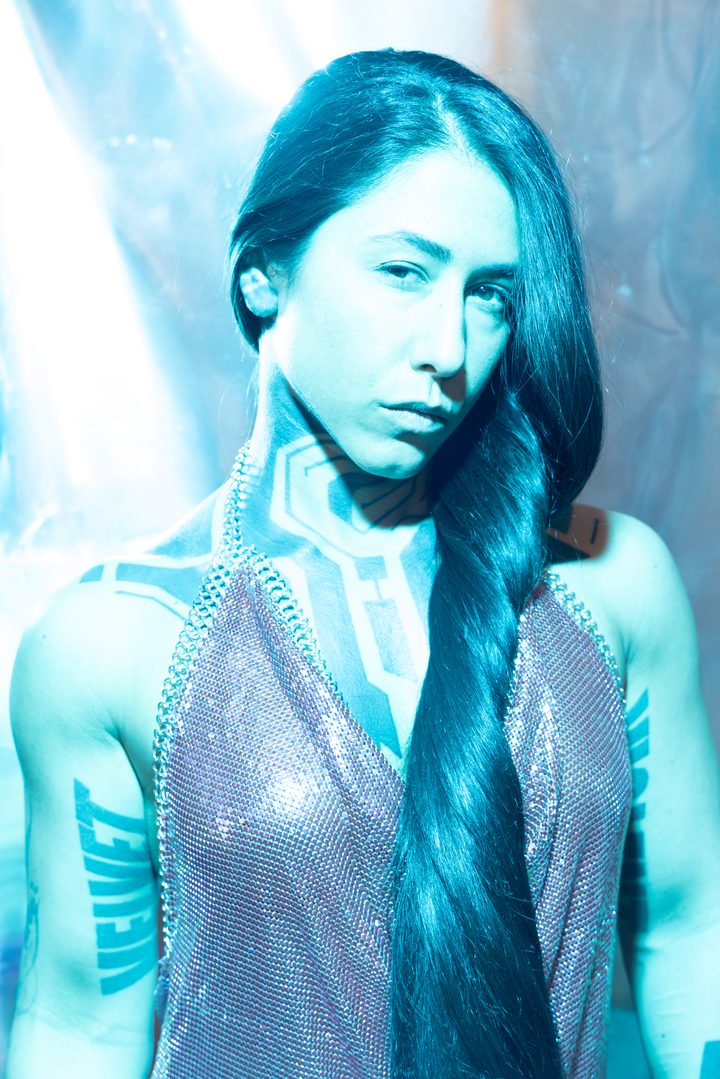 An icy-blue beauty portrait, mesh and a long braid, geometric blackwork lit by gelled strobe and held tack-sharp.
