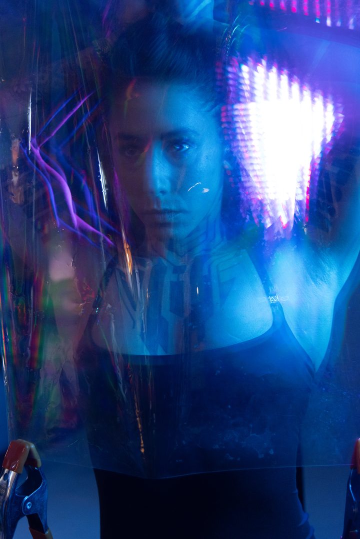 A magenta-and-violet portrait seen through a sheet of scratched plastic, the surface fracturing the face into soft color.