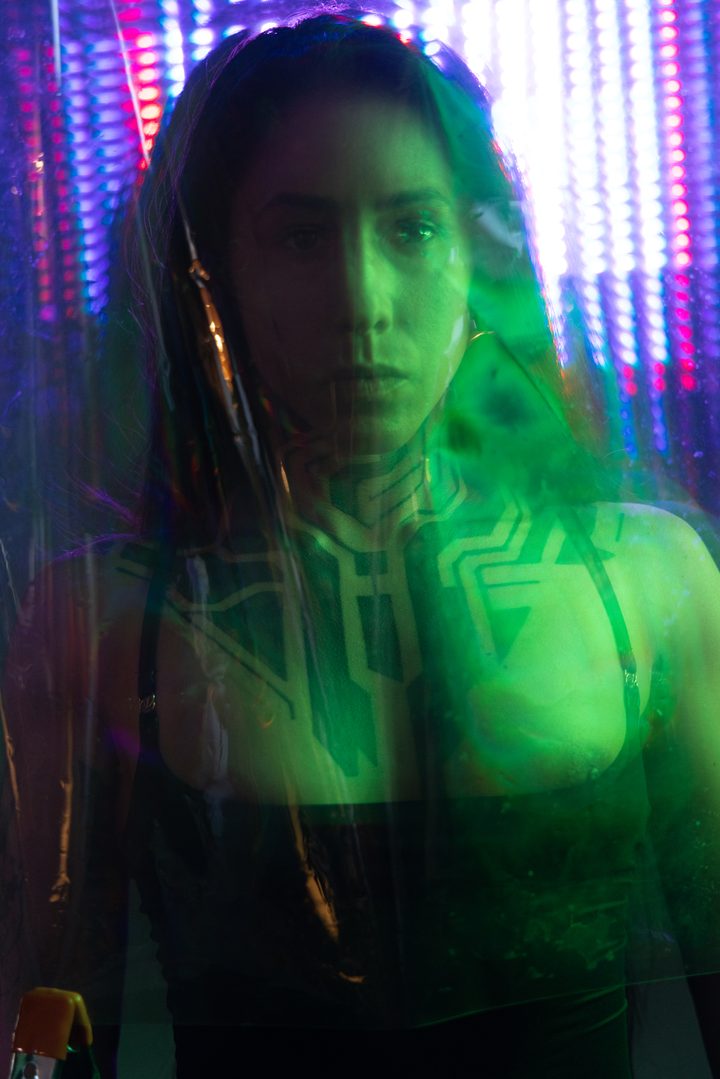 A figure behind scratched acetate in blue and white light, projected linework doubling across the body through the surface.