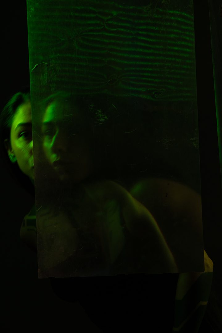 A figure behind a wall of fine projected light, warm highlights raining down the frame across the body and the dark ground.