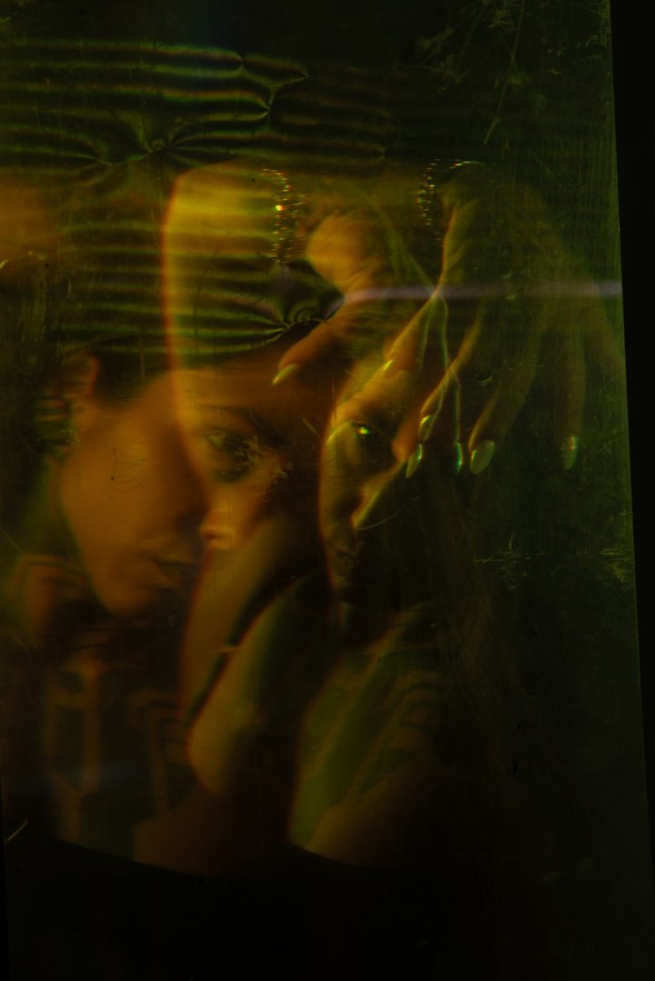 A reclining figure under a wash of projected light, warm and cool highlights scattered across the body and the frame.
