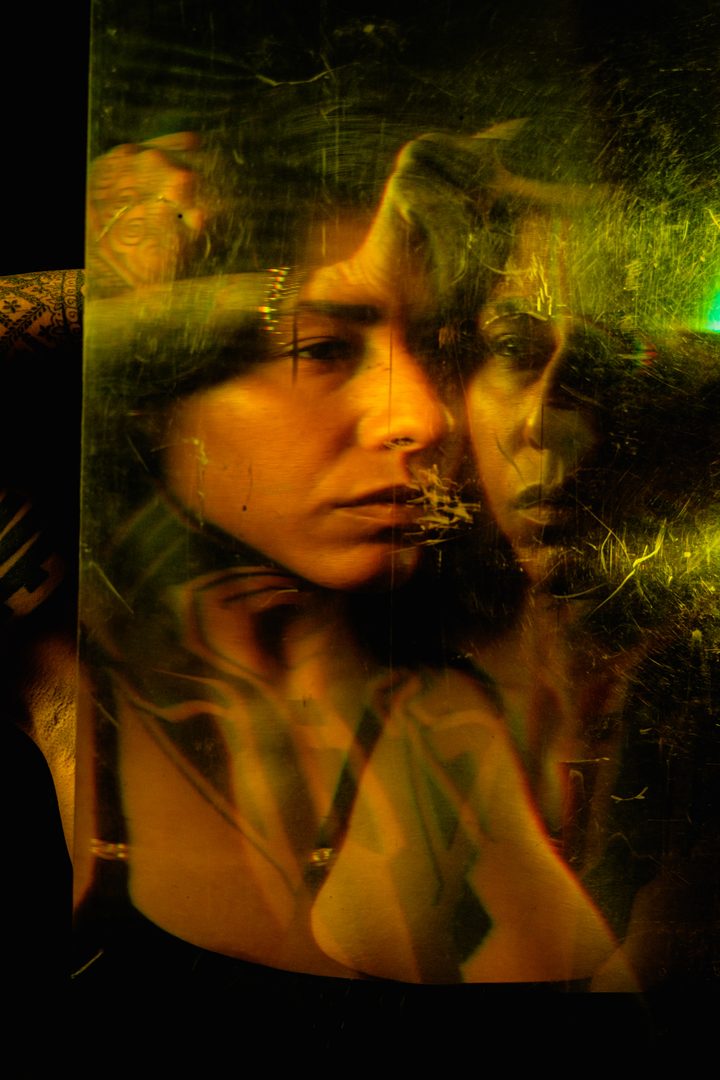 A double portrait in green and gold, the figure split and ghosted by long-exposure motion across a fine projected grid.
